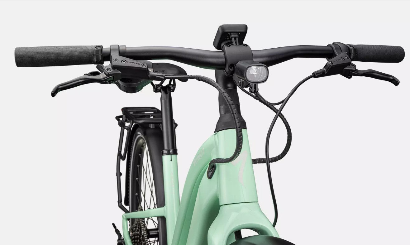 Close up view of the front of a light green Specialized Vado electric bicycle with black components on a white background.