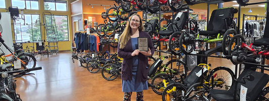 Hostel Shoppe owner, Breanna, poses with the NBDA People's Choice Award in front of a row of recumbent trikes.