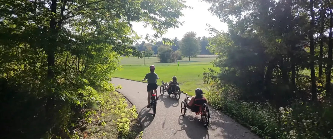 A biker and two trikers ride down a bike path.