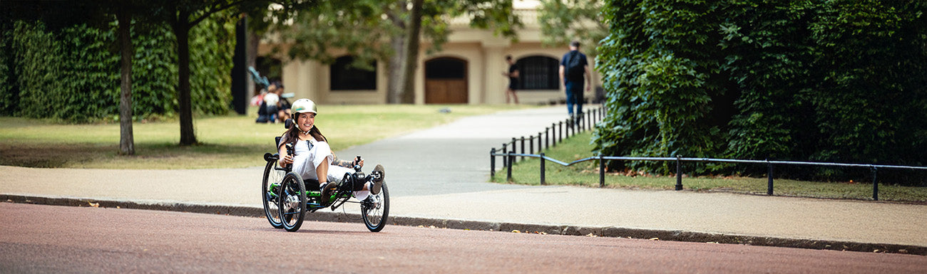 A woman rides a recumbent trike through a park like setting.