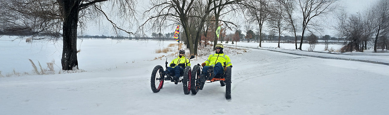 Two riders ride fat trikes in the snow.