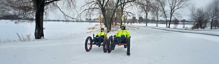 Two riders ride fat trikes in the snow.