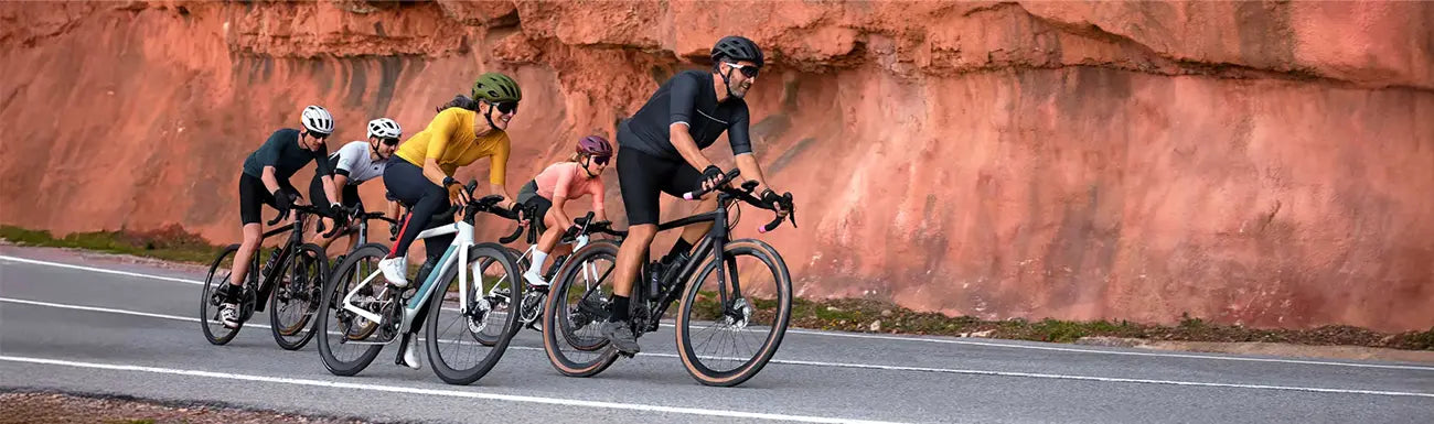 A group of road bikers ride along a rock wall.