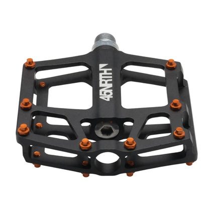 Angled top view of the 45NRTH Heiruspecs 9/16 Inch Aluminum Black Platform Pedal with orange studs against a white background.