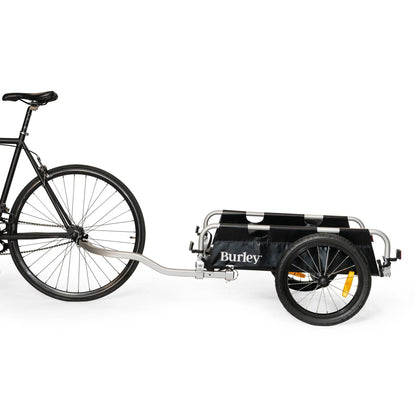 Side view of the Burley Flatbed Cargo Trailer, shown attached to a bicycle, on a white background.