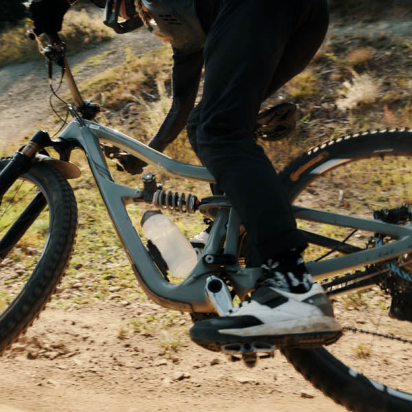 Biker rides a trail with Fidlock TWIST 750 Compact Bottle and Bike Base attached to her mountain bike frame.