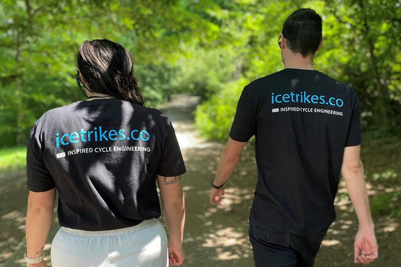 Back view Front view of a man and woman wearing a black t-shirt with the words icetrikes.co in light blue lettering across the shoulders, and Inspired Cycle Engineering in white lettering below that. 