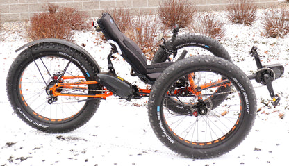 Right profile view of orange ICE full fat recumbent trike in the snow.