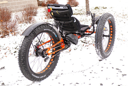 Right back angle view of an ICE full fat recumbent trike with black seat, tires, battery, and rear fender and orange and black frame. 