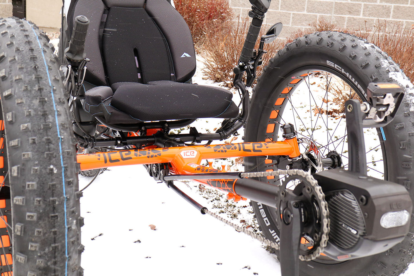 Front right view of an ICE orange Full Fat recumbent trike with a closeup of the Shimano motor and orange frame. 