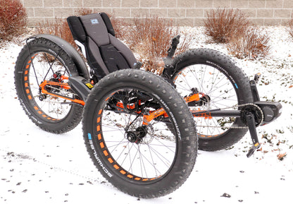 Front right side view of an orange ICE full fat recumbent trike in the snow. 