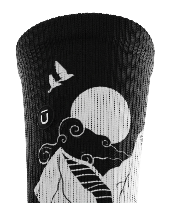 Cuff area of black and white socks with mountain and forest scene.  Small black circular patch with Outway logo stitched on top third of cuff.