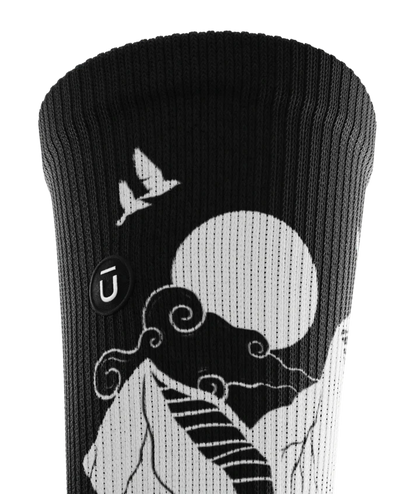 Cuff area of black and white socks with mountain and forest scene.  Small black circular patch with Outway logo stitched on top third of cuff.