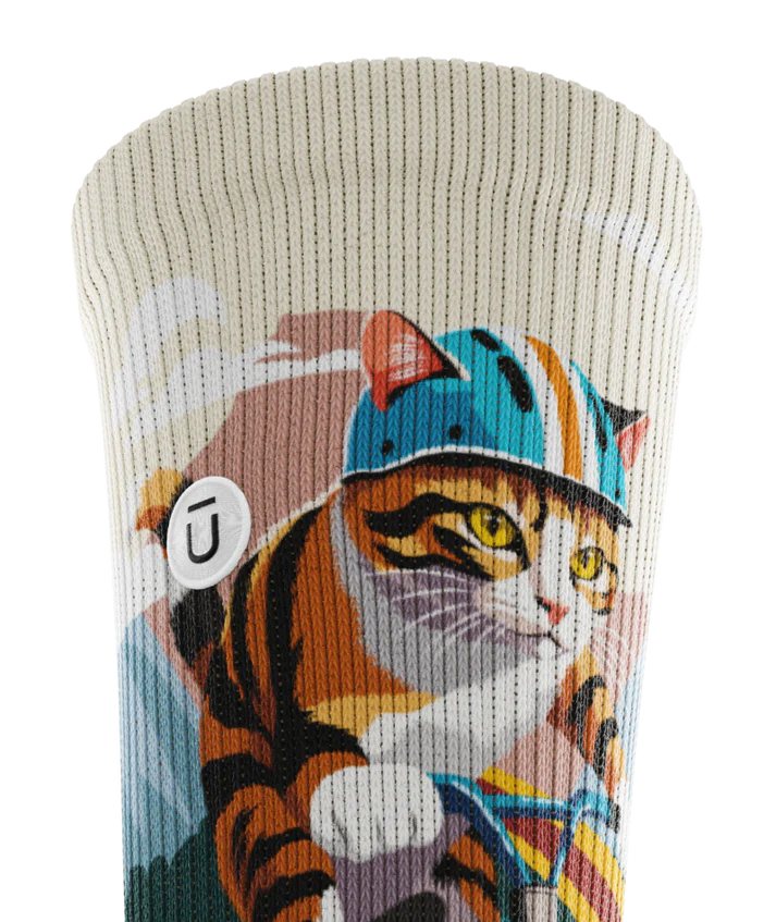 Close up of cuff of a multicolored sock with cats wearing helmets riding bikes in a race. Small white circular patch with Outway logo stitched into top third of cuff