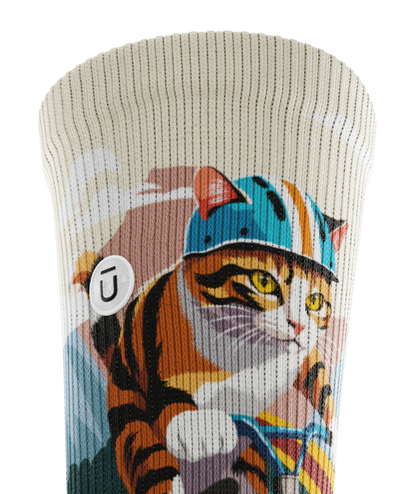 Close up of cuff of a multicolored sock with cats wearing helmets riding bikes in a race. Small white circular patch with Outway logo stitched into top third of cuff