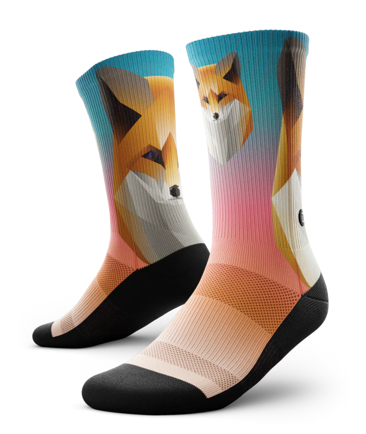 Multicolored pair of socks with geometric sock head. Background of sock is teal blue at the top fading to light orange near toes. Sole of socks is black