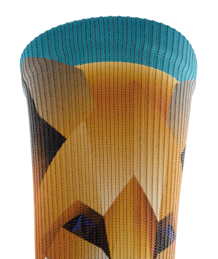 Top cuff of multicolored sock with geometric sock head. Background of sock is teal blue 