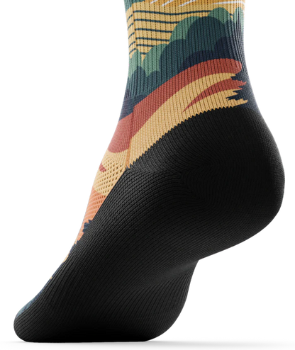 Bottom black sole of a multicolored sock depicting mountain forest scene with person riding bike on a trail.