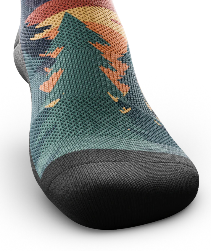 Top and toe area of a multicolored sock depicting mountain forest scene with person riding bike on a trail.