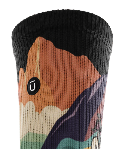 Top cuff view of a multicolored sock depicting mountain forest scene with person riding bike on a trail.  Small black circular patch with Outway logo stitched on top third of cuff. 