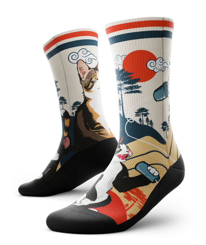 Multicolored pair of socks with black and white cat talking into a can connected with a string to another calico cat.  Asian inspired background of trees and sun. Black soles