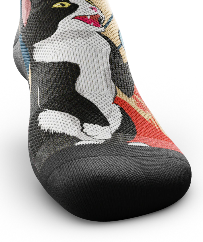Top toe view of a Multicolored sock with black and white cat talking into a can.  Black soles