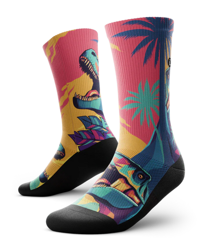Multicolored  pair of socks with T-rex dinosaurs and palm trees on main part of sock, black soles. 