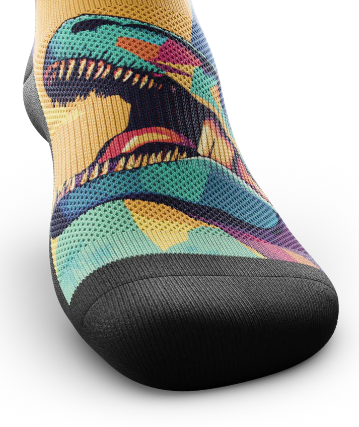 Top toe area of Multicolored sock with T-rex dinosaurs and palm trees on main part of sock, black soles. 