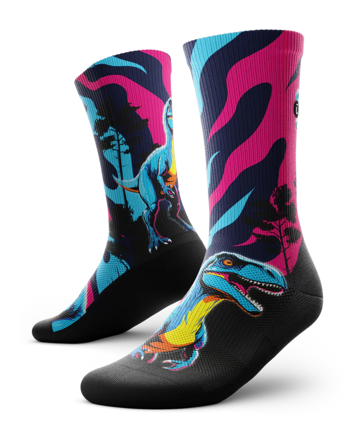 Multicolored pink, blue and black pair of socks with velociraptors, black trees and black soles. 