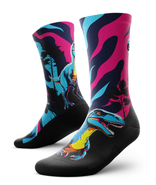 Multicolored pink, blue and black pair of socks with velociraptors, black trees and black soles. 
