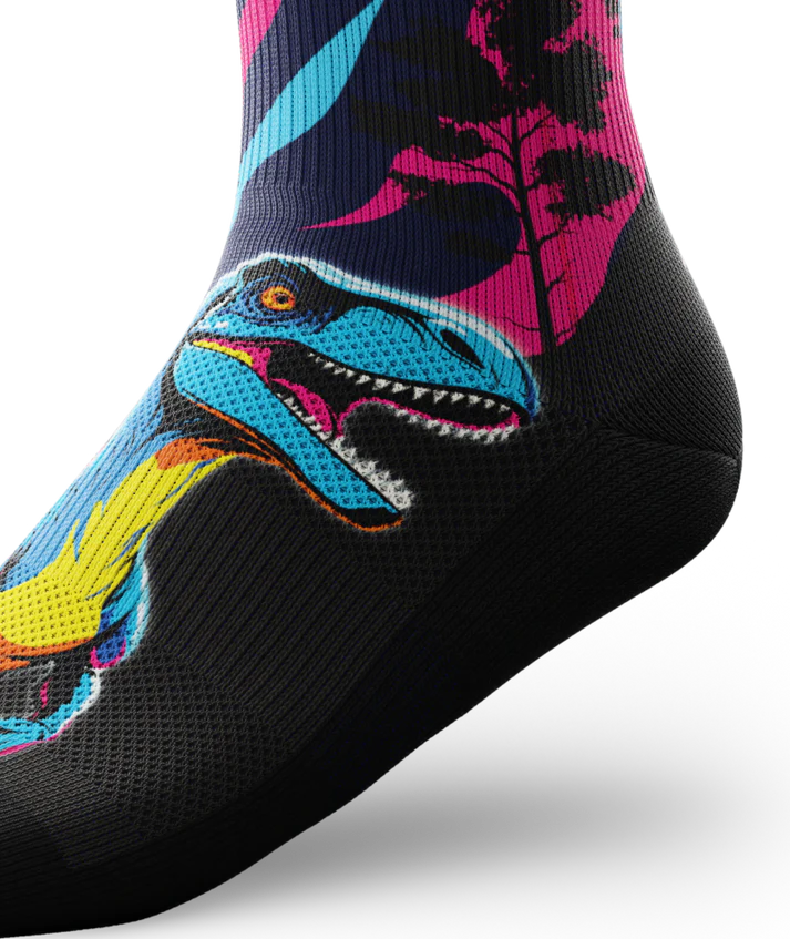 Side ankle view of multicolored pink, blue and black sock with velociraptors, black trees and black soles. 