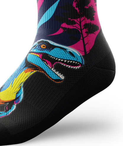 Side ankle view of multicolored pink, blue and black sock with velociraptors, black trees and black soles. 