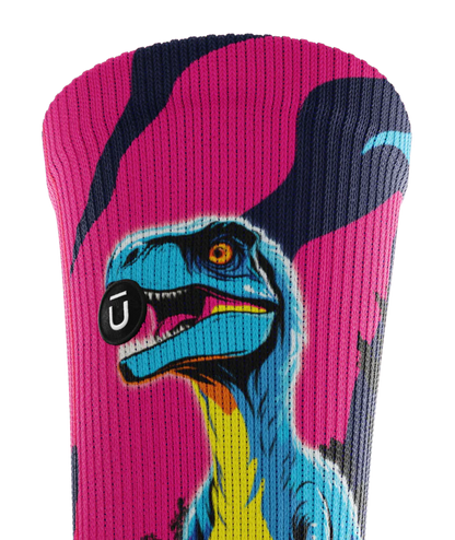 Top cuff of multicolored pink, blue and black pair of socks with velociraptors, and black trees. Small black circular patch with Outway logo on top third of cuff. 