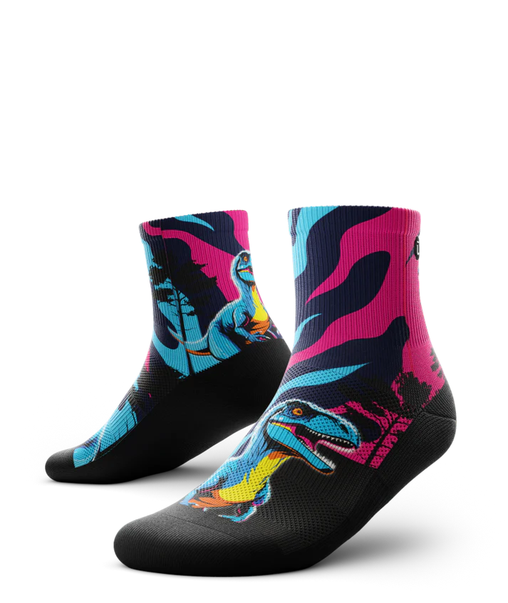 Multicolored pink, blue and black pair of socks with velociraptors, black trees and black soles. 