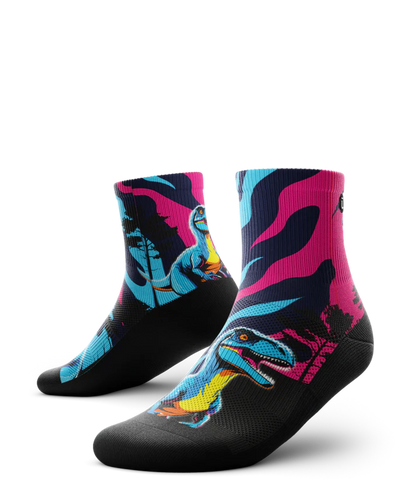 Multicolored pink, blue and black pair of socks with velociraptors, black trees and black soles. 