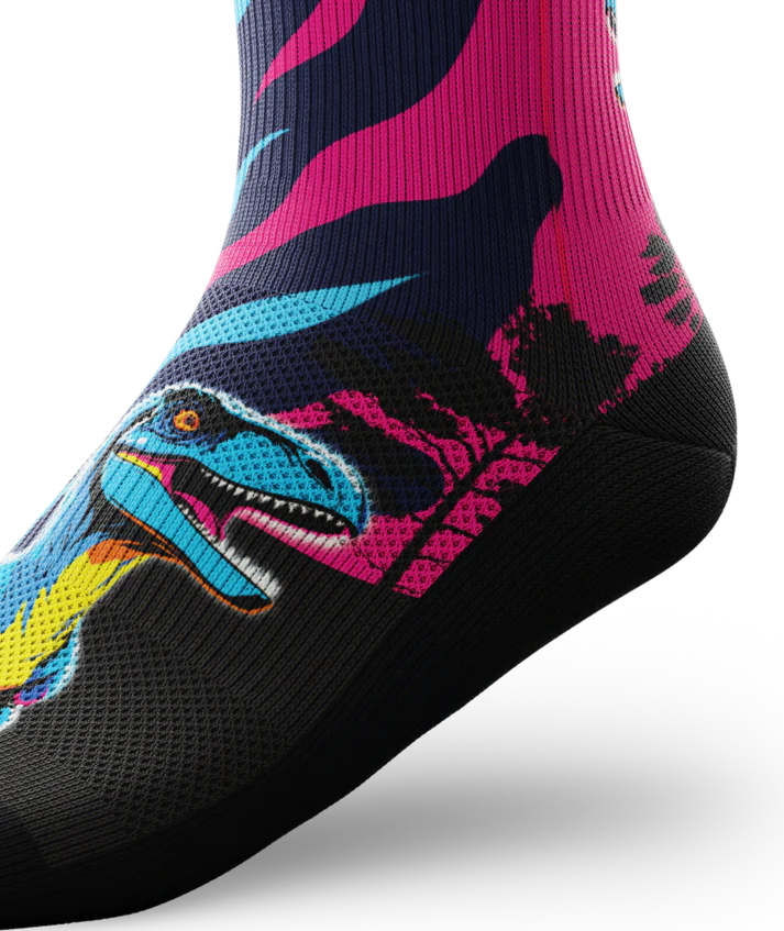 Side ankle view of multicolored pink, blue and black sock with velociraptors, black trees and black soles. 