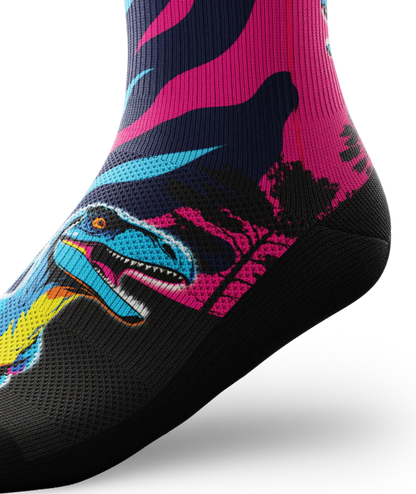 Side ankle view of multicolored pink, blue and black sock with velociraptors, black trees and black soles. 
