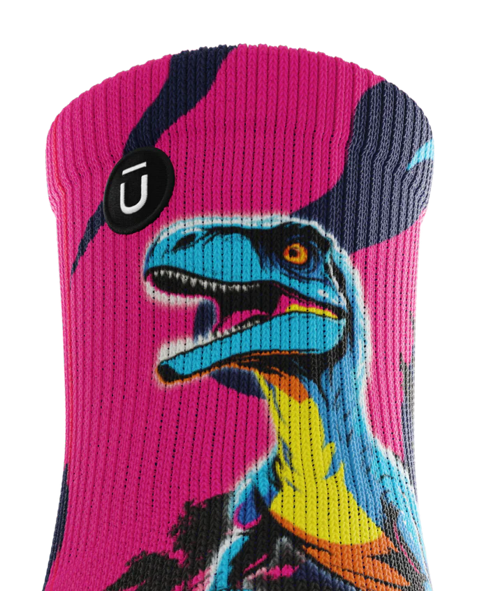 Top cuff of multicolored pink, blue and black pair of socks with velociraptors, and black trees. Small black circular patch with Outway logo on top third of cuff. 