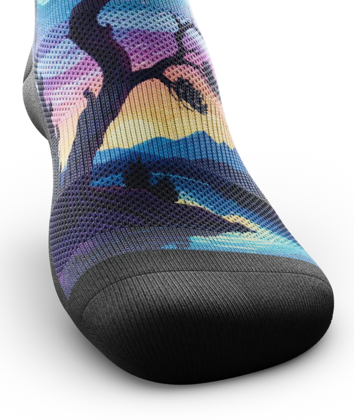 Top toe view of multicolored sock with colorful northern lights in the ski over a mountain lake with trees silhouetted.  