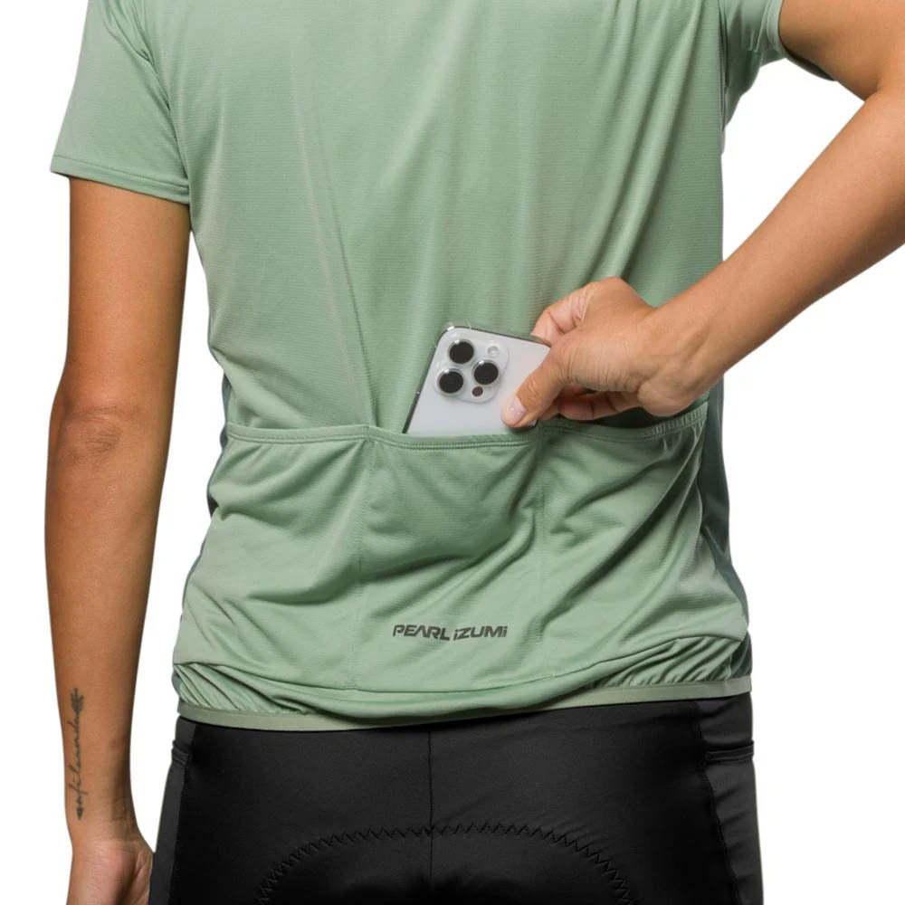 Studio image of Pearl Izumi Sugar Jersey Green Bay being worn by model who is putting a white phone into the middle of three pockets across the lower back. 