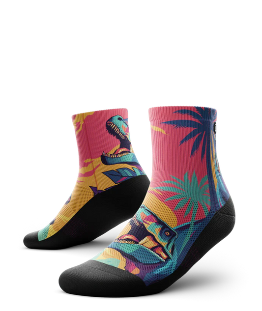 Multicolored  pair of socks with T-rex dinosaurs and palm trees on main part of sock, black soles. 