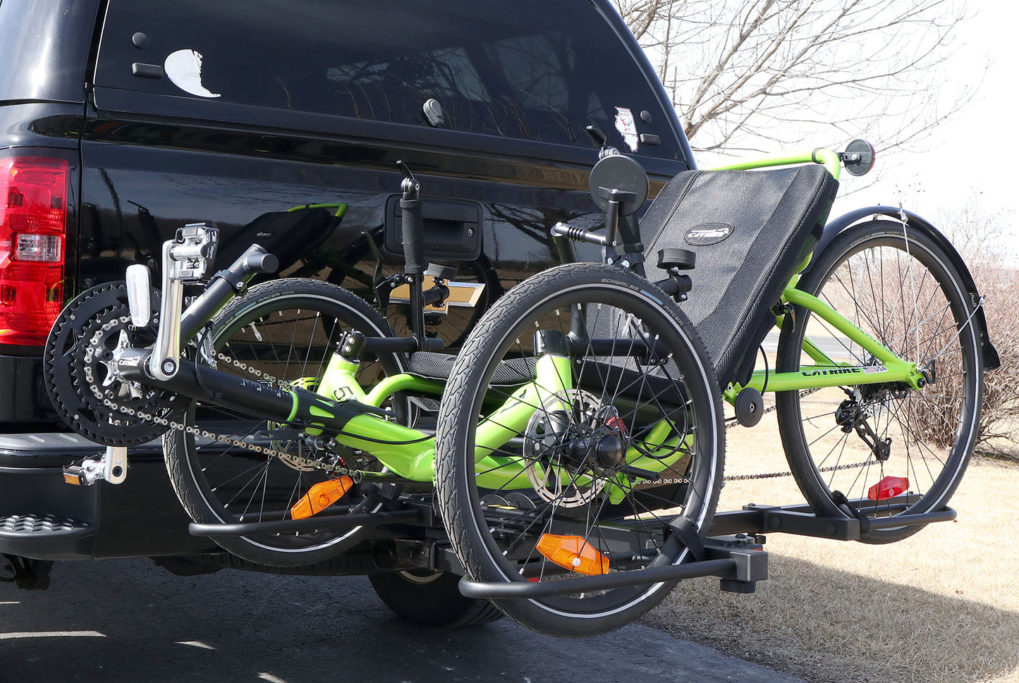 Angled view of the Sunlite HRT-100 Trike Auto Rack for 2-inch Receivers mounted on the hitch on a pickup truck with a green Catrike on the rack in an outdoor setting.