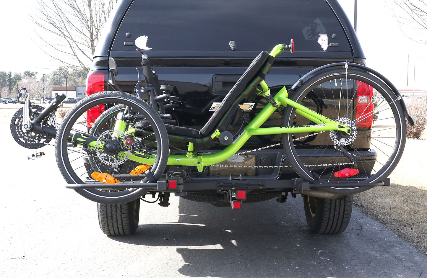 View of the Sunlite HRT-100 Trike Auto Rack for 2-inch Receivers mounted on the hitch on a pickup truck with a green Catrike on the rack in an outdoor setting.