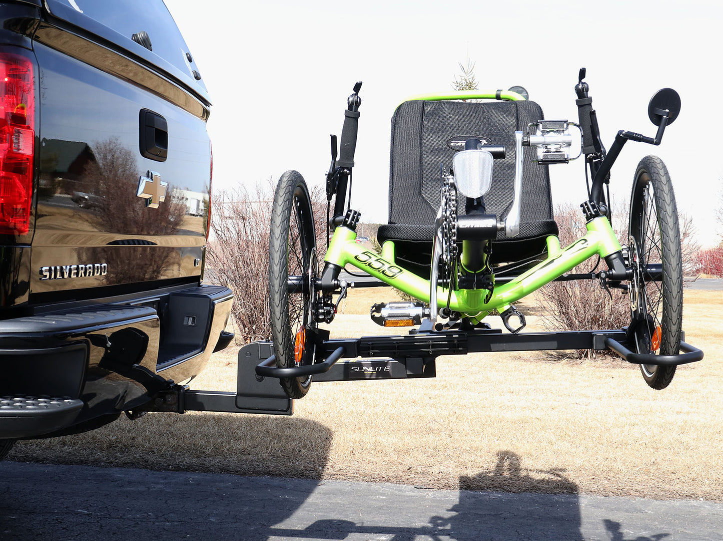 Side view of the Sunlite HRT-100 Trike Auto Rack for 2-inch Receivers mounted on the hitch on a pickup truck with a green Catrike on the rack in an outdoor setting.