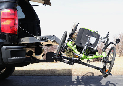 Tilted down view of the Sunlite HRT-100 Trike Auto Rack for 2-inch Receivers mounted on the hitch on a pickup truck to allow access to the tailgate with a green Catrike on the rack in an outdoor setting.