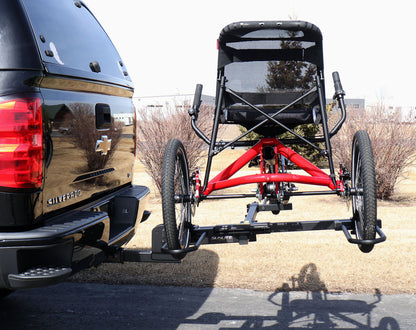 Side view of the Sunlite HRT-100 Trike Auto Rack for 2-inch Receivers mounted on the hitch on a pickup truck  with a red Hase Trigo on the rack in an outdoor setting.