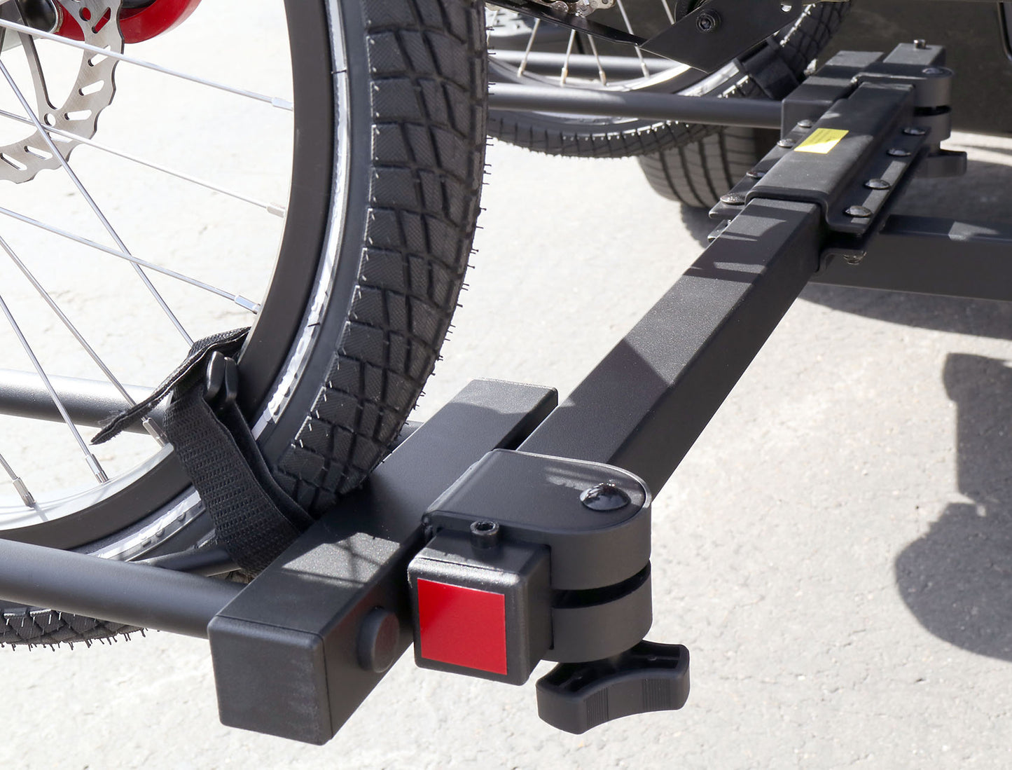 Close up view of the moveable wheel tray and velcro strap on the Sunlite HRT-100 Trike Auto Rack for 2-inch Receivers mounted on the hitch on a black pickup truck in an outdoor setting.