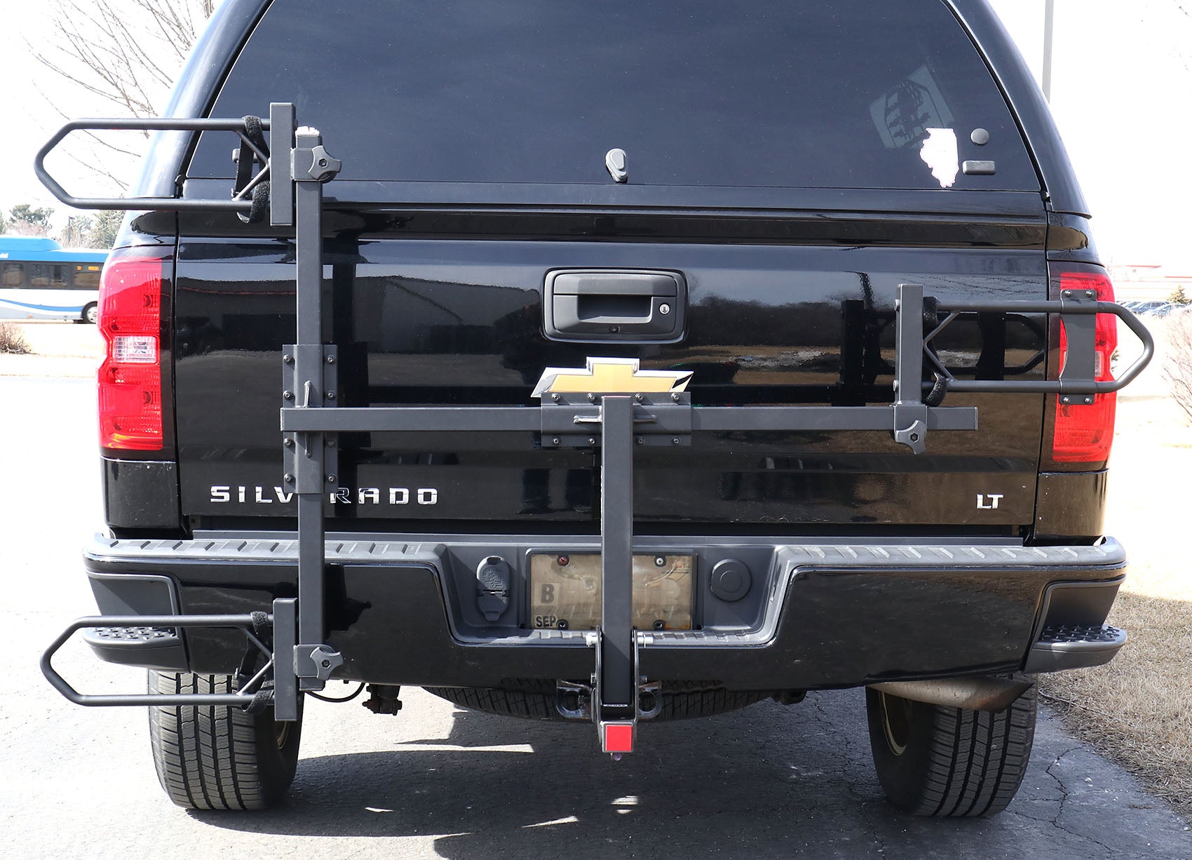Folded up view of the Sunlite HRT-100 Trike Auto Rack for 2-inch Receivers mounted on the hitch on a black pickup truck in an outdoor setting.