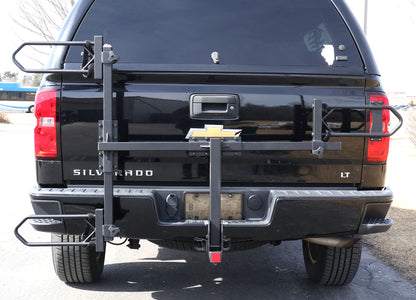 Folded up view of the Sunlite HRT-100 Trike Auto Rack for 2-inch Receivers mounted on the hitch on a black pickup truck in an outdoor setting.