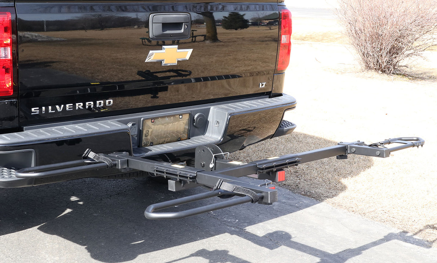 Angled view of the Sunlite HRT-100 Trike Auto Rack for 2-inch Receivers mounted on the hitch on a black pickup truck in an outdoor setting.